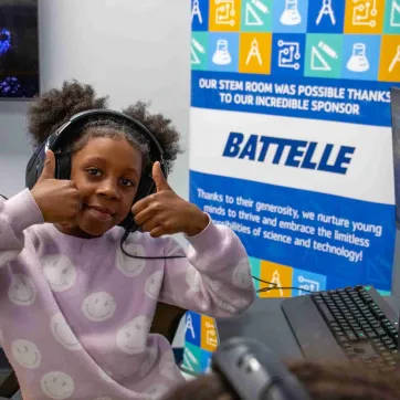 student smiles with thumbs up in front of a Battelle sign