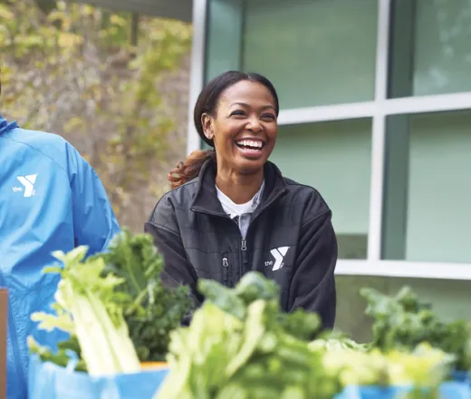 women in YMCA jacket hands out produce at local food drive